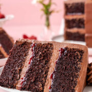 A slice of chocolate raspberry cake on a white plate with two raspberries next to it.