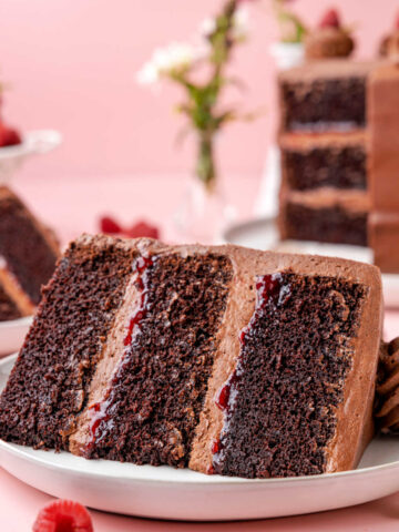 A slice of chocolate raspberry cake on a white plate with two raspberries next to it.