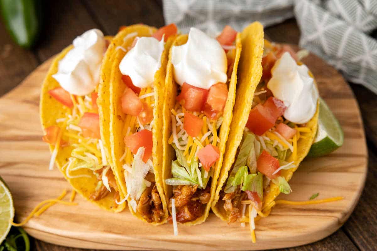 Four shredded chicken tacos topped with lettuce tomatoes and sour cream.
