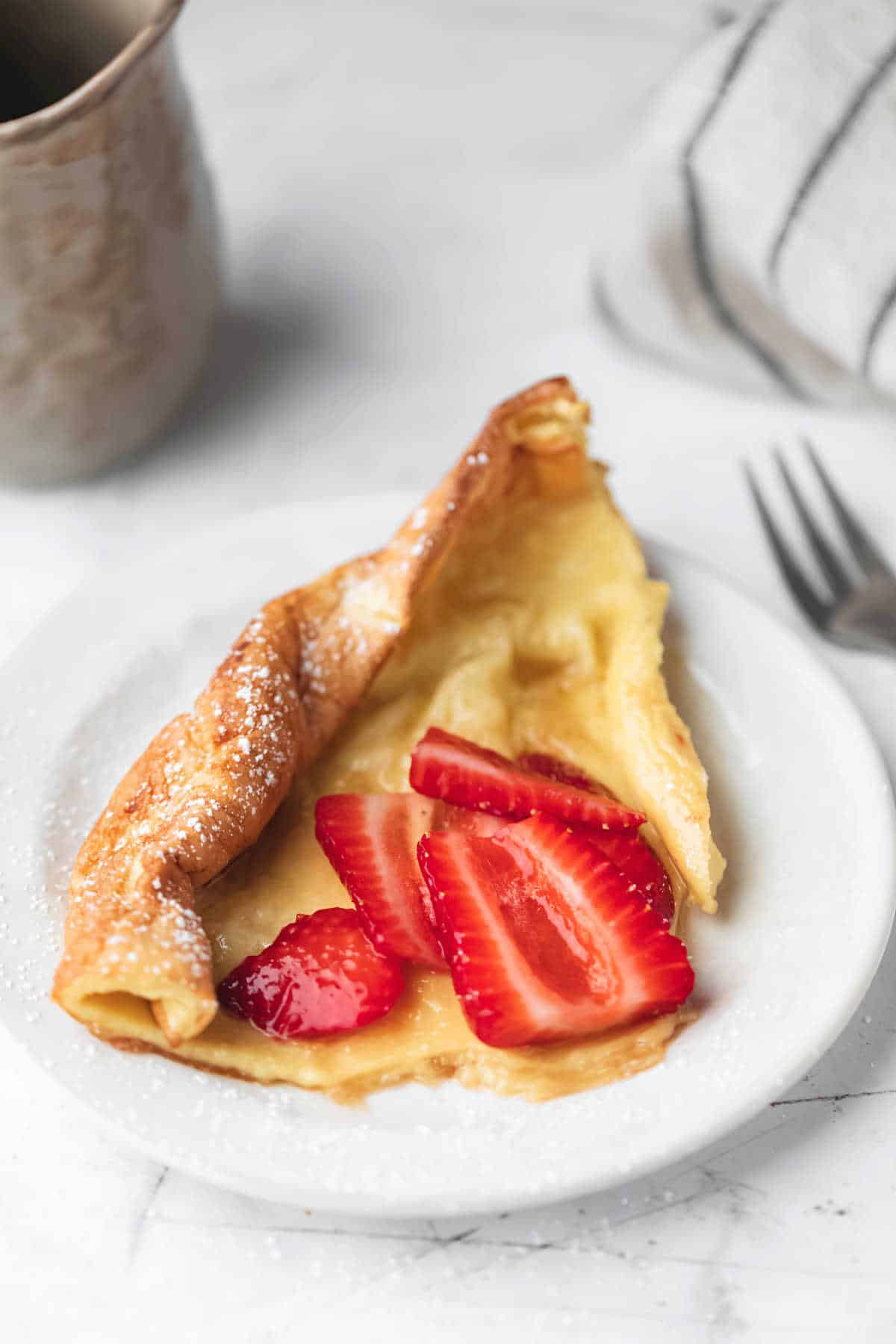 A Piece of German pancake on a plate next to a fork. 