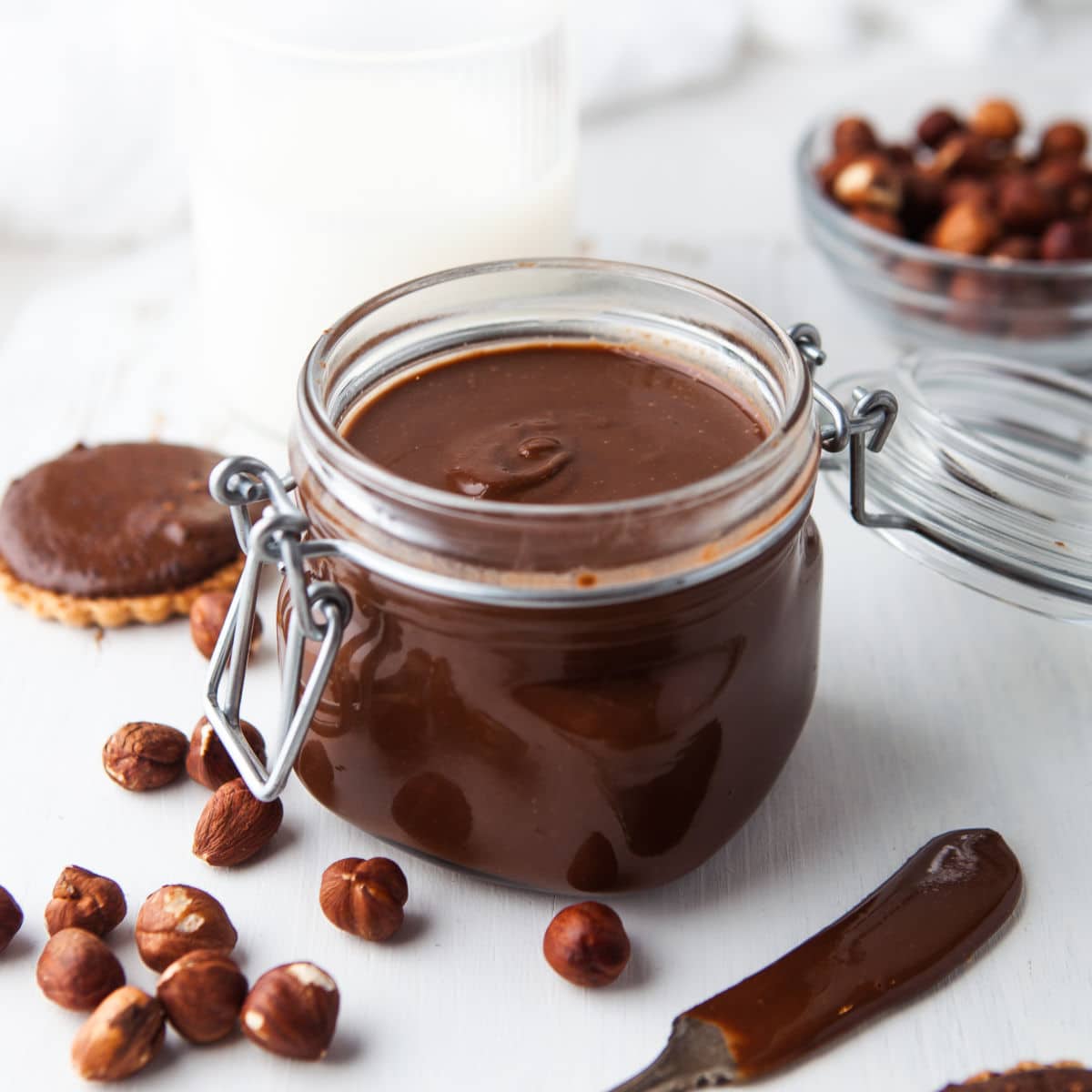 Glass jar of Nutella next to a bowl of hazelnuts.