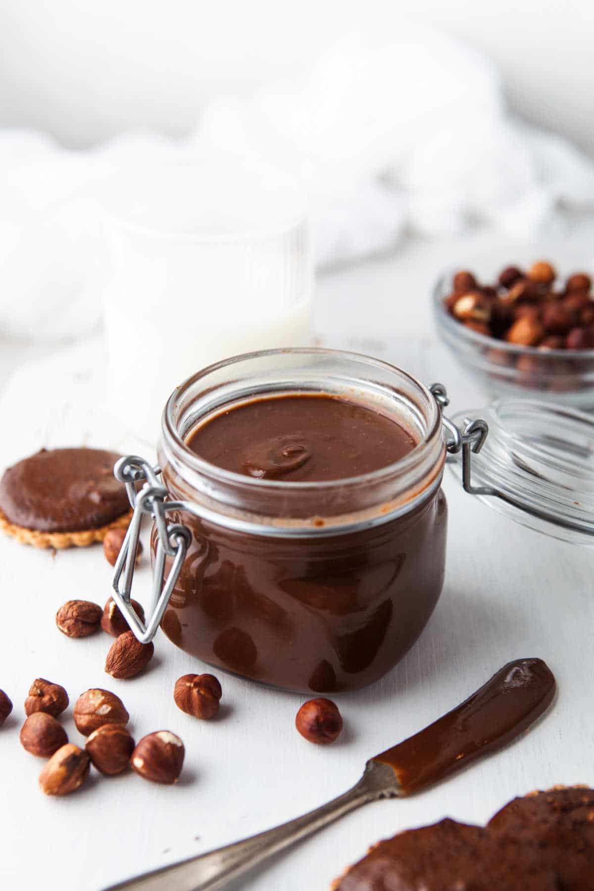 Glass jar of homemade nutella next to hazelnuts and a knife with nutella on it.