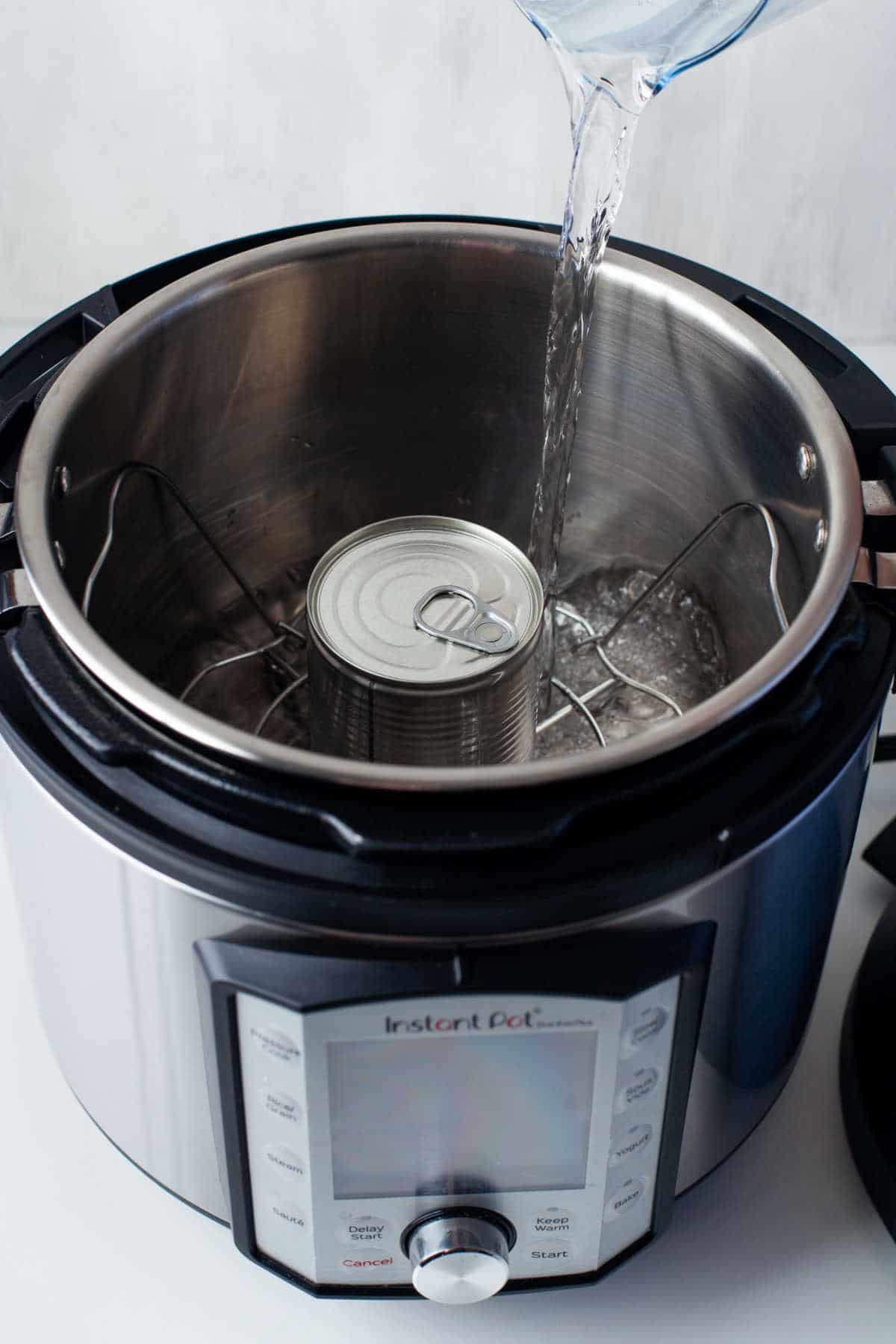 Water pouring over a can and into an instant pot inner pot.