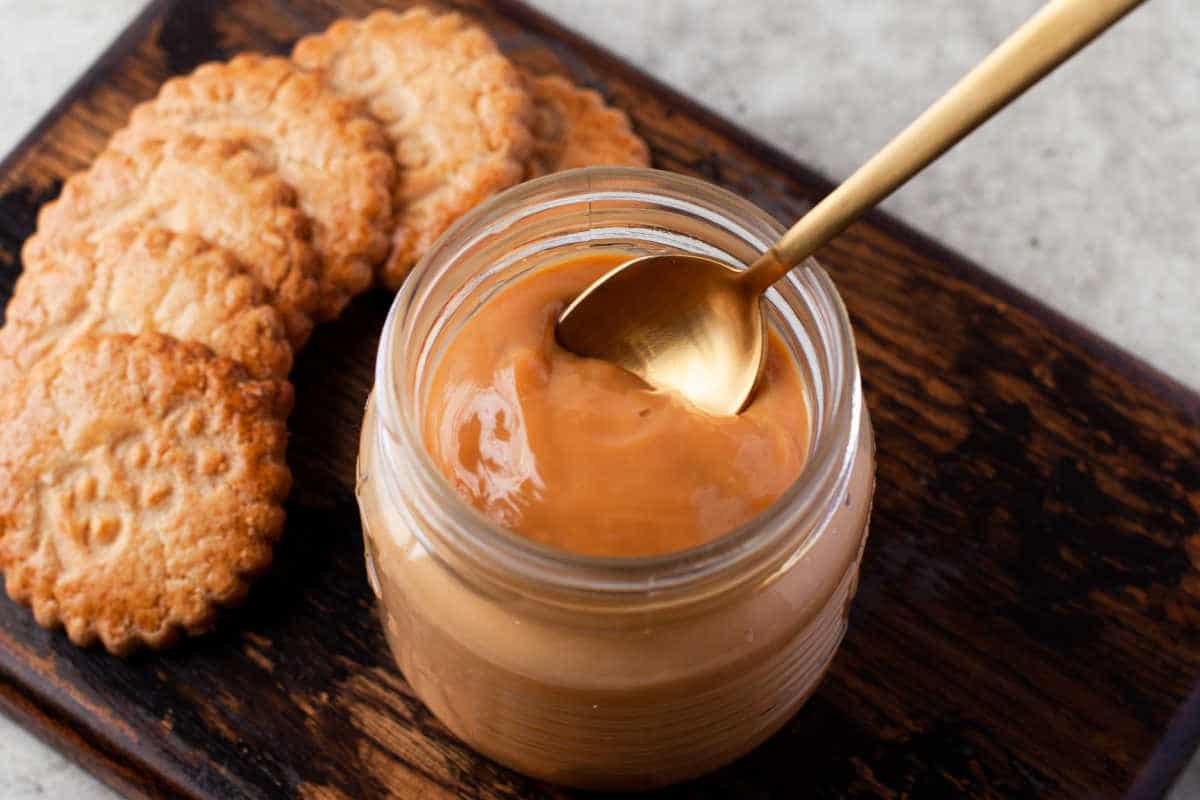 A gold spoon in a jar of dulce de leche next to cookies. 