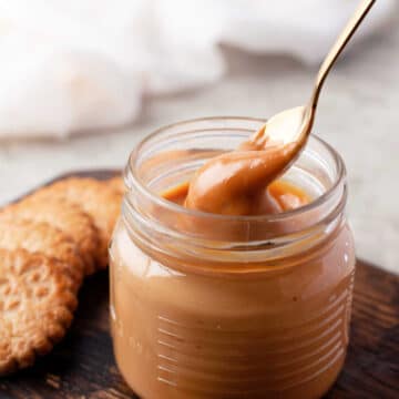 A golden spoon dipping up dulce de leche from a glass jar.