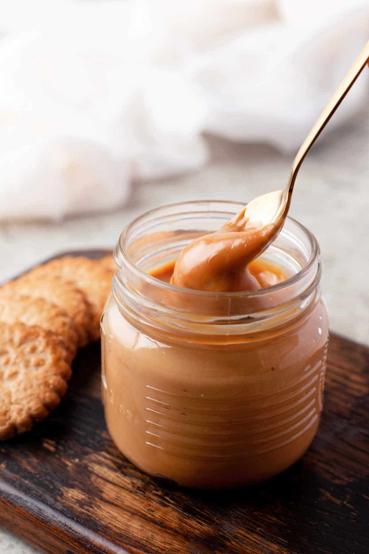 A golden spoon dipping up dulce de leche from a glass jar.