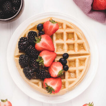 Belgian waffle on a white plate topped with fresh berries.
