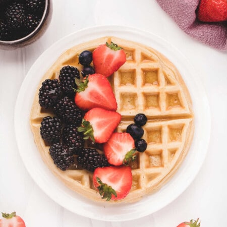 Belgian waffle on a white plate topped with fresh berries.