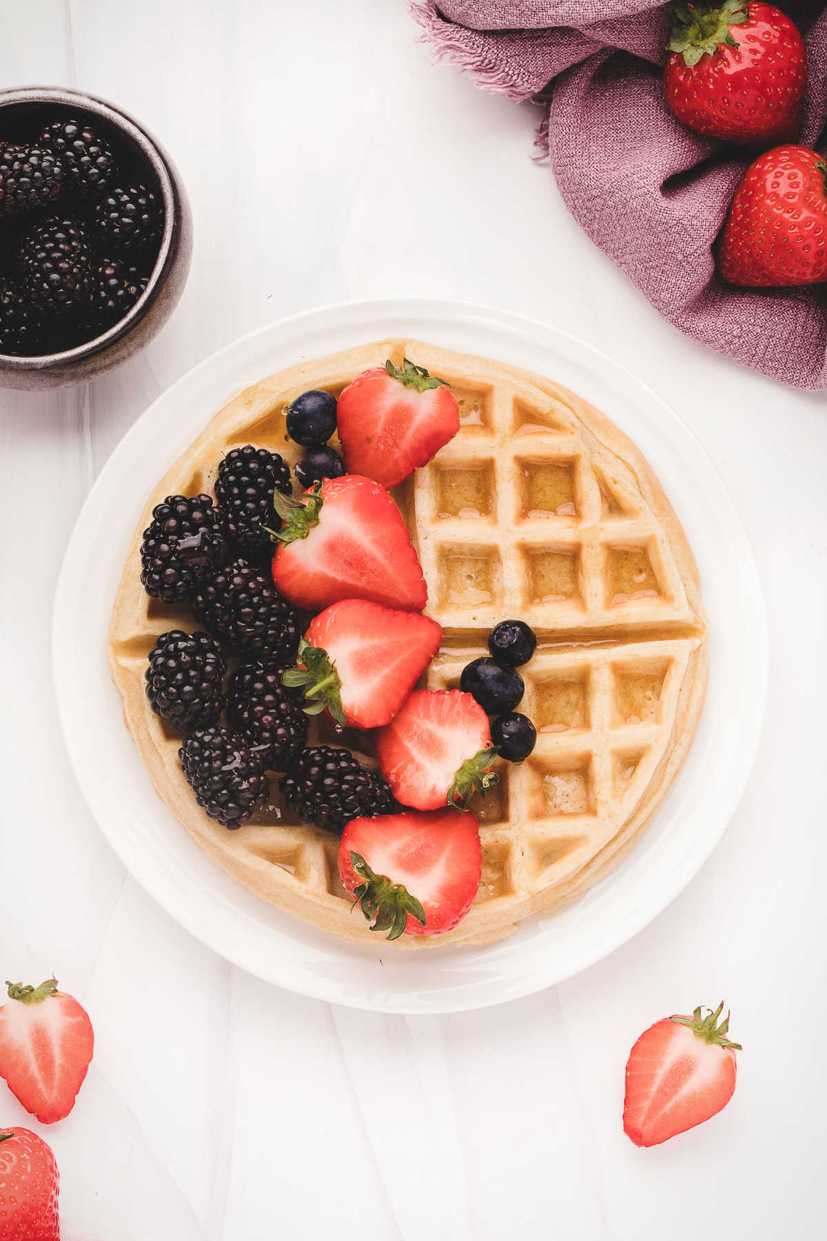 Belgian waffle on a white plate topped with fresh berries. 