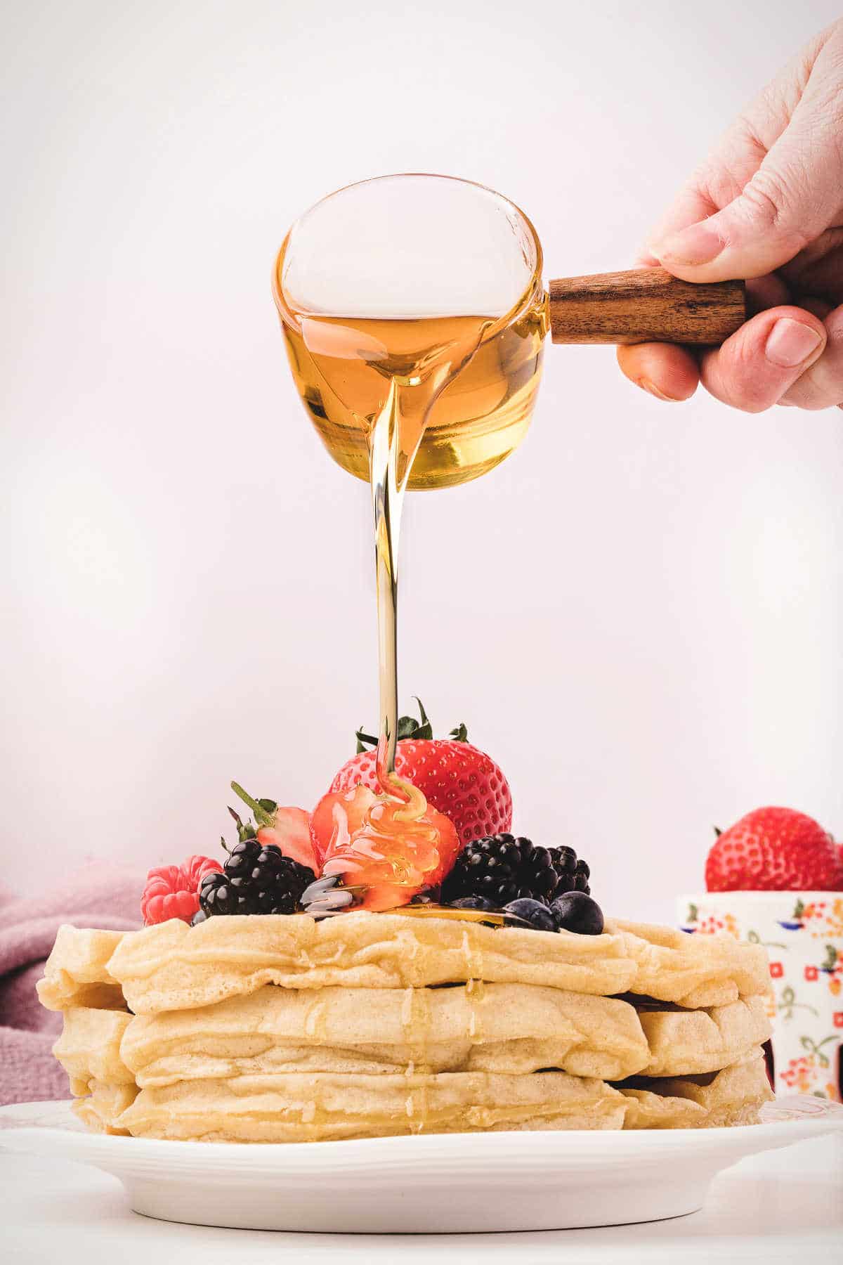 Syrup pouring onto a stack of Belgian waffles.