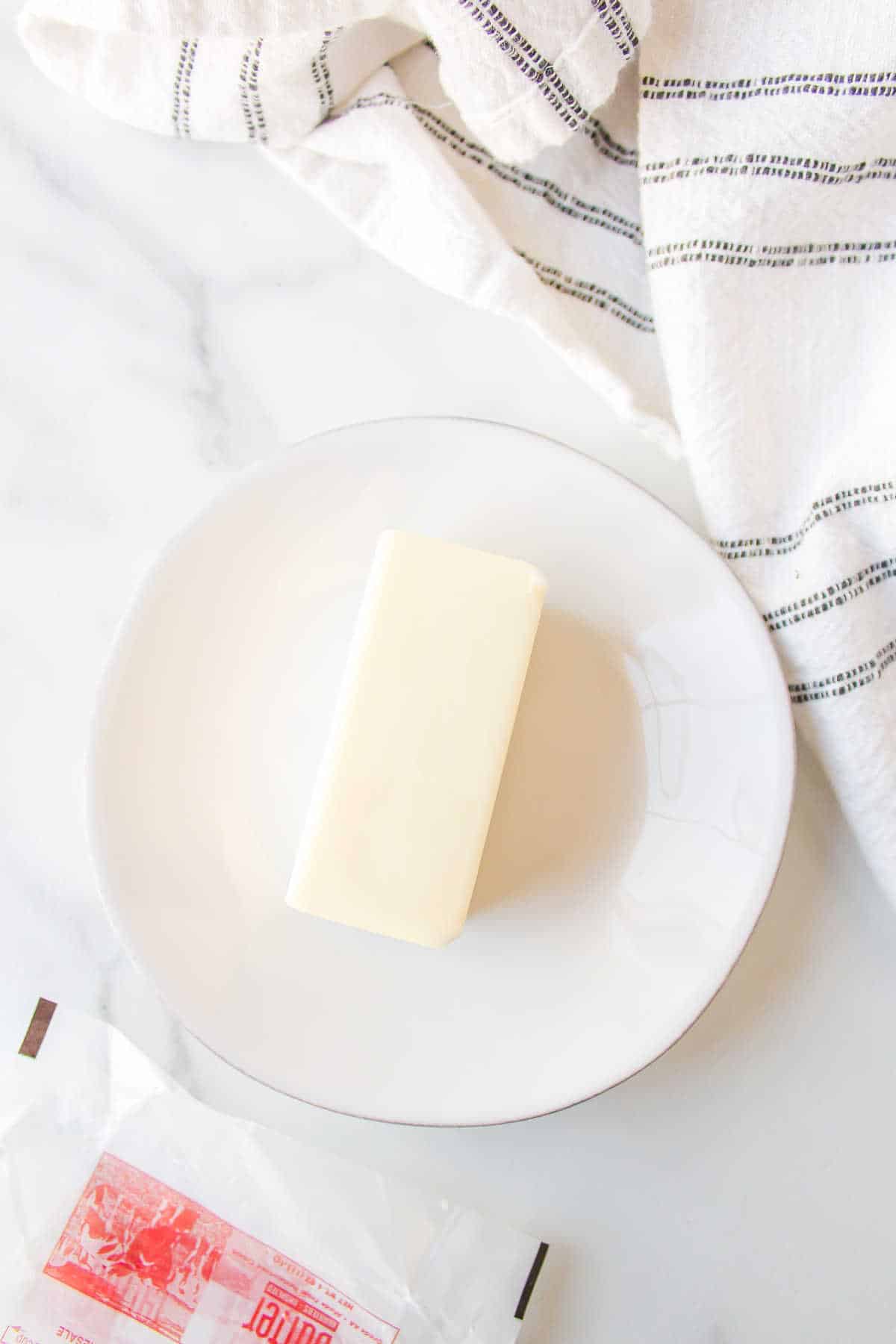 A stick of butter on a white plate on a counter. 