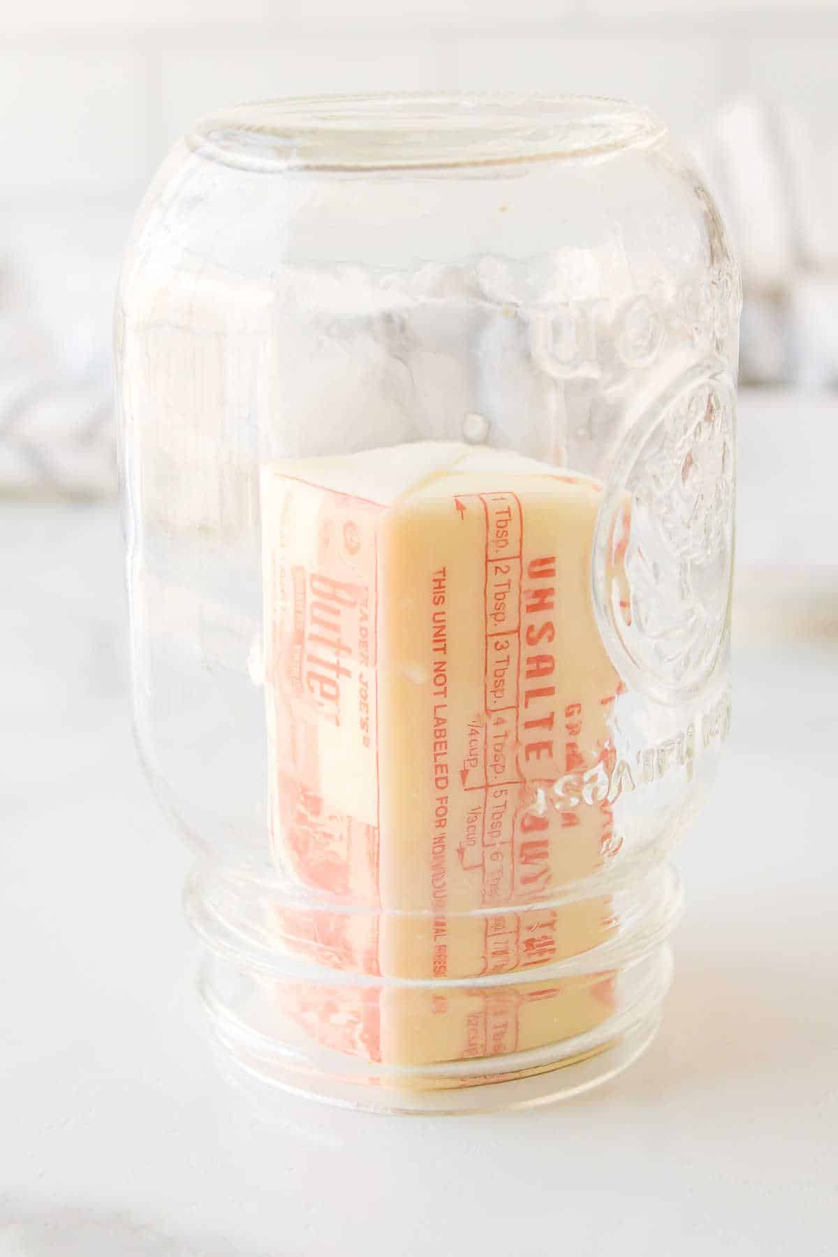 A clear glass jar sitting over a stick of butter.