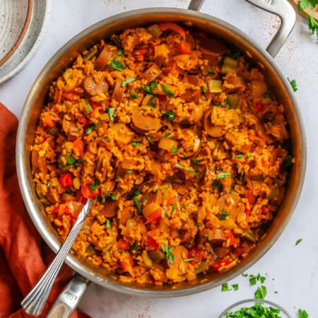 A skillet of Cajun sausage and rice with a silver spoon in it.