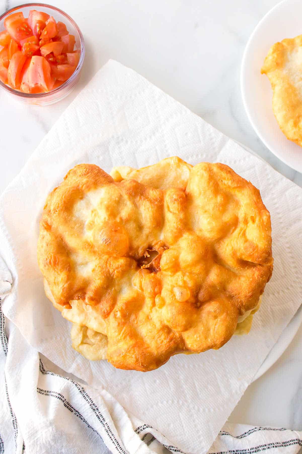 A piece of fry bread on a paper towel lined plate.