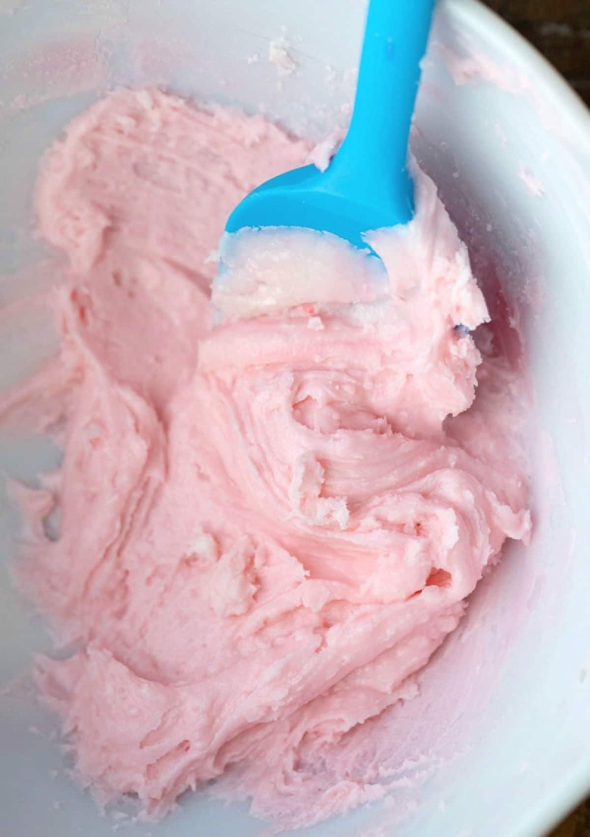 A bowl of pink frosting with a spatula in it. 