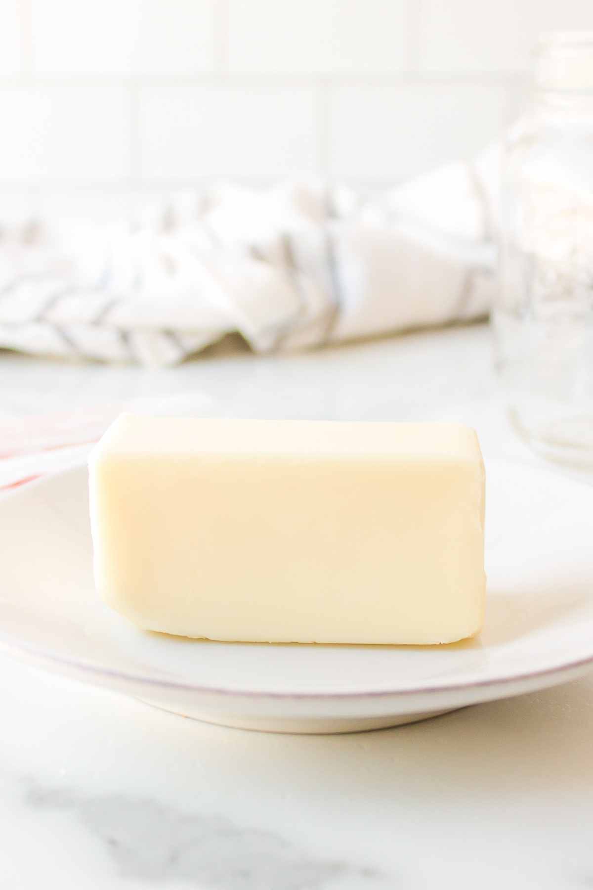 An unwrapped stick of butter on a white plate. 