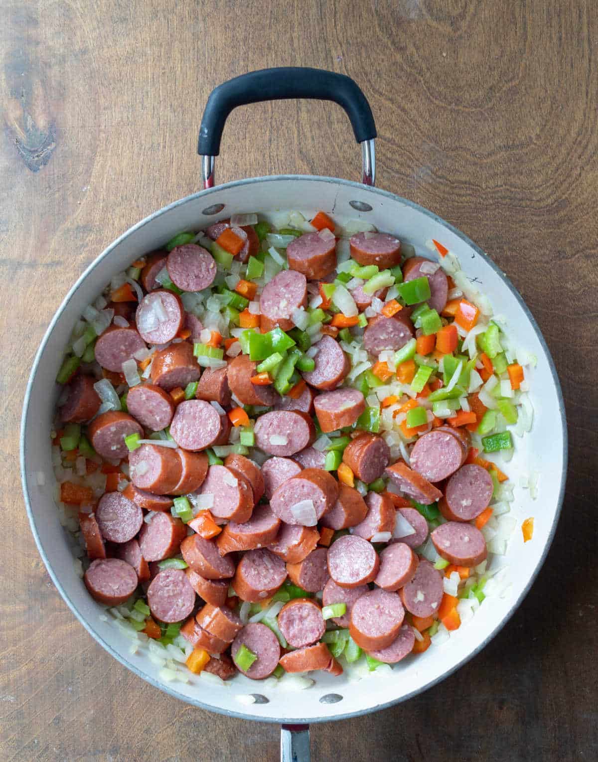 Sliced kielbasa and vegetables cooking in a large skillet. 