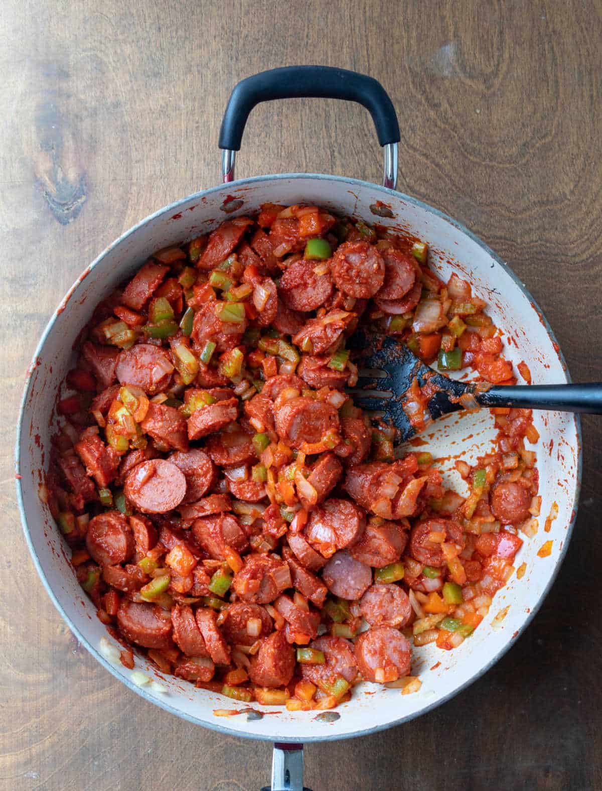 Kielbasa vegetables and tomato paste cooking in a skillet. 