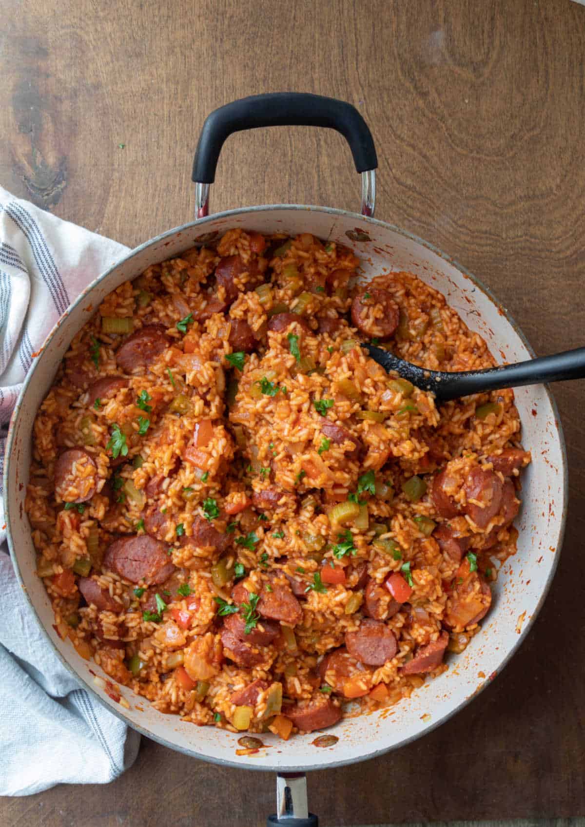 A skillet of Cajun sausage and rice with a black spoon in it. 