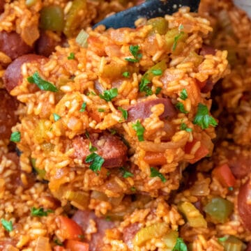 A spoon scooping up Cajun sausage and rice from a skillet.