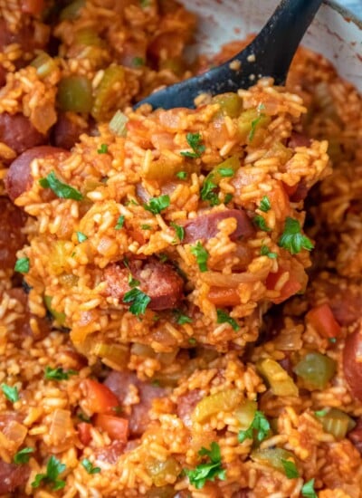 A spoon scooping up Cajun sausage and rice from a skillet.