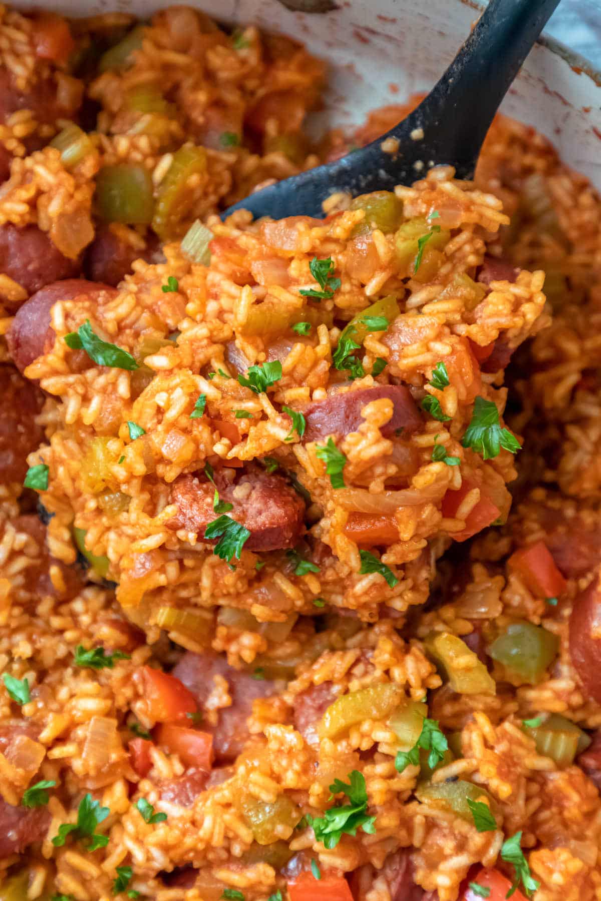 A spoon scooping up Cajun sausage and rice from a skillet.