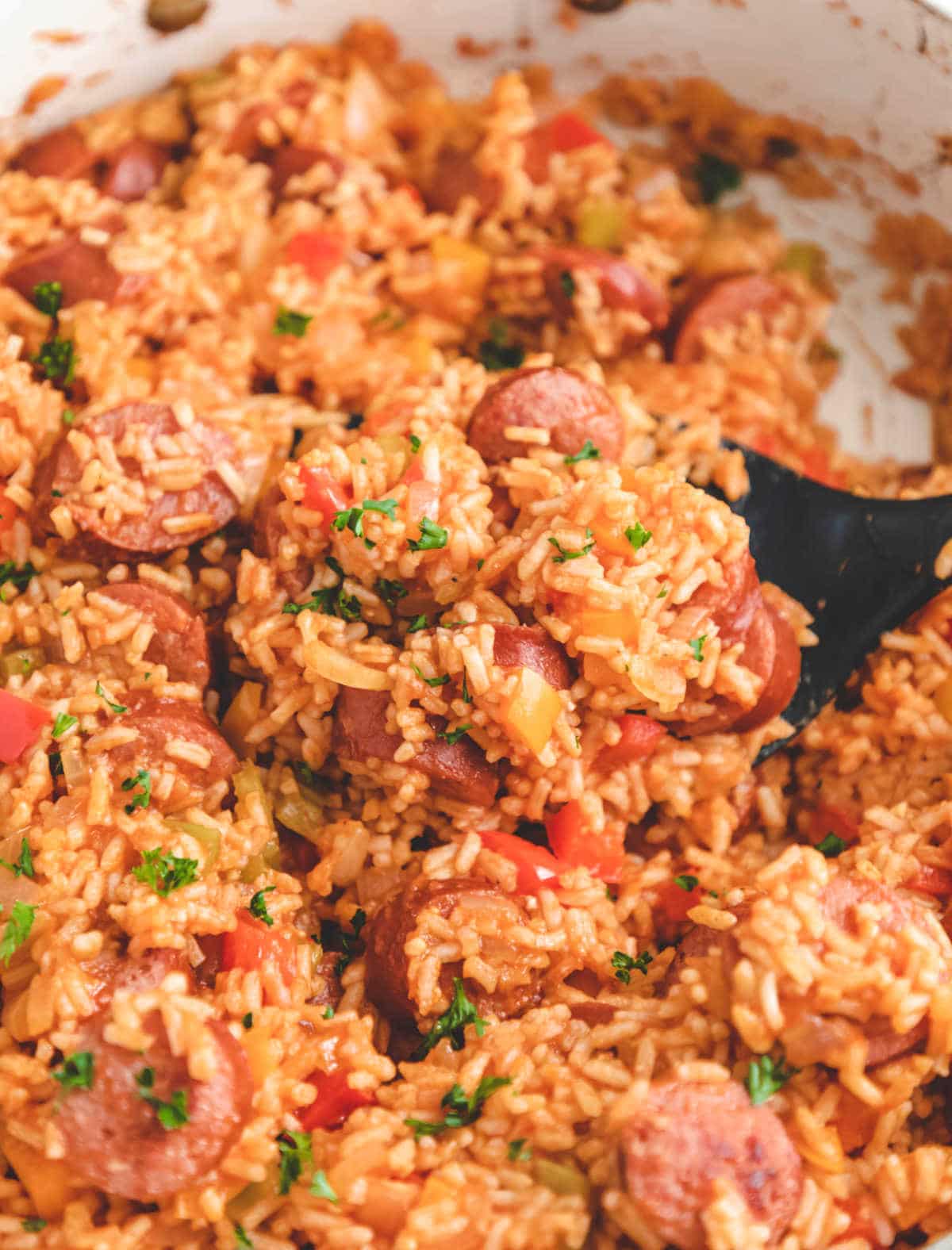 A black spoon stirring Cajun sausage and rice in a skillet. 