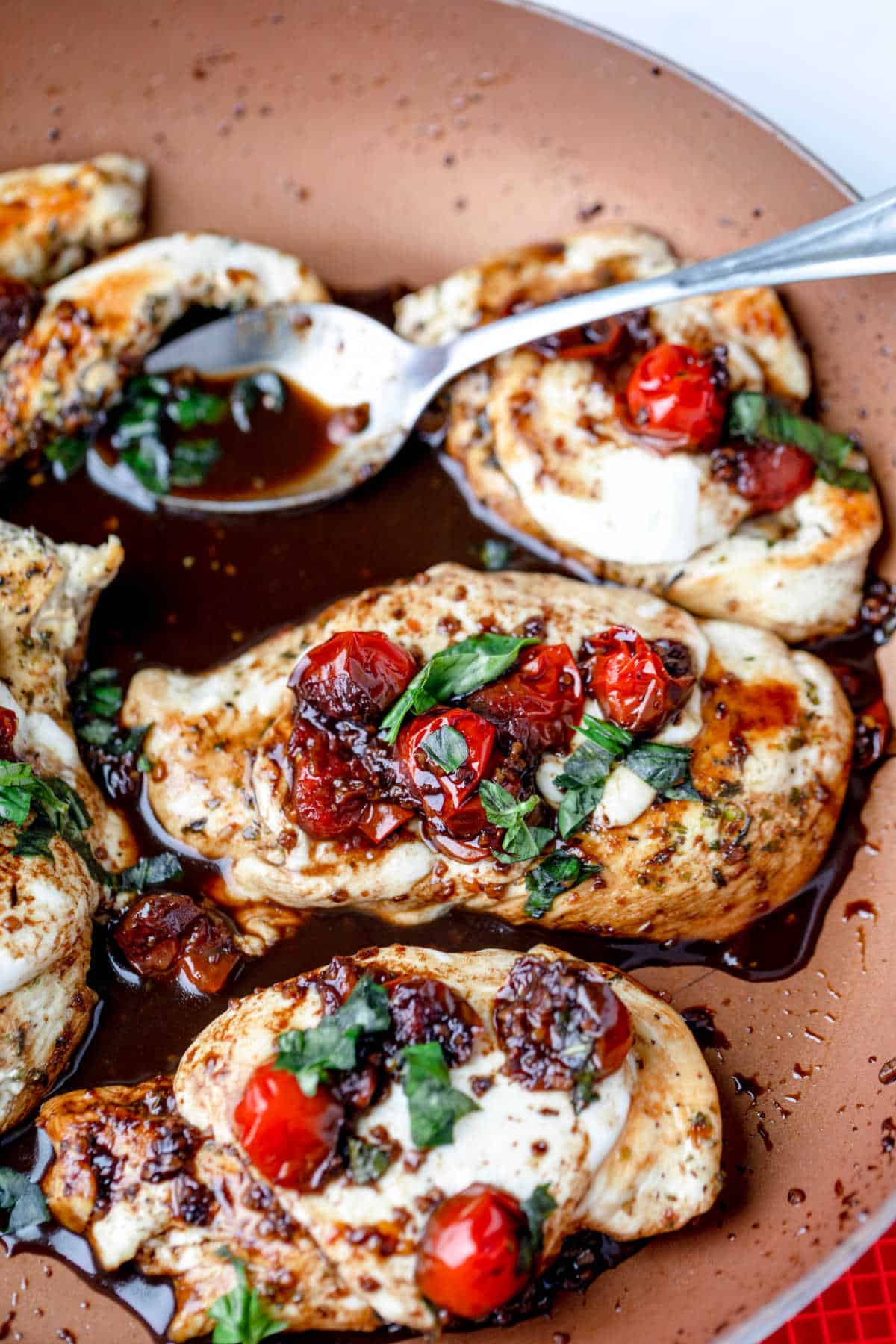 A spoon holding balsamic glaze next to caprese chicken.