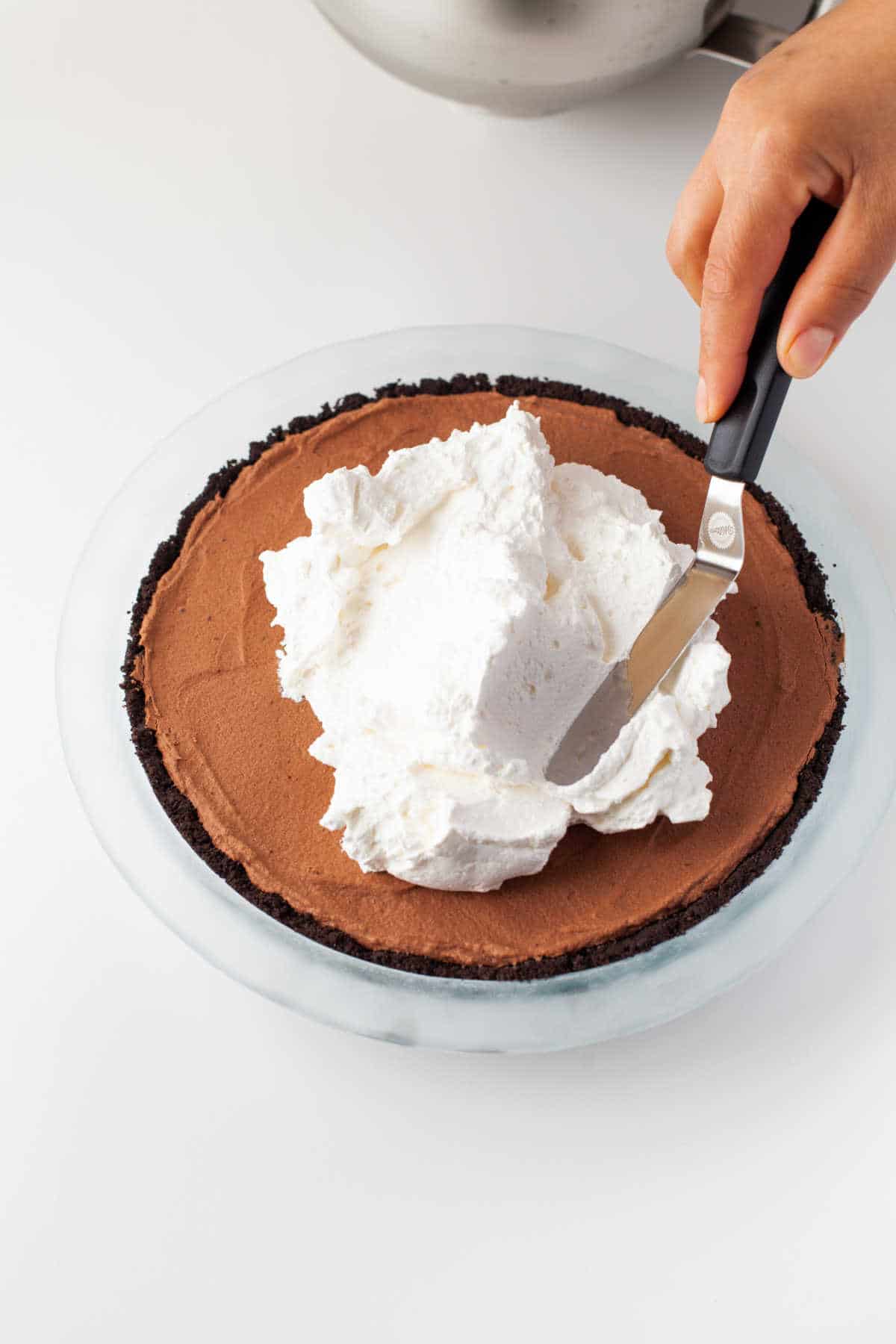 A spatula spreading whipped cream over the pie.
