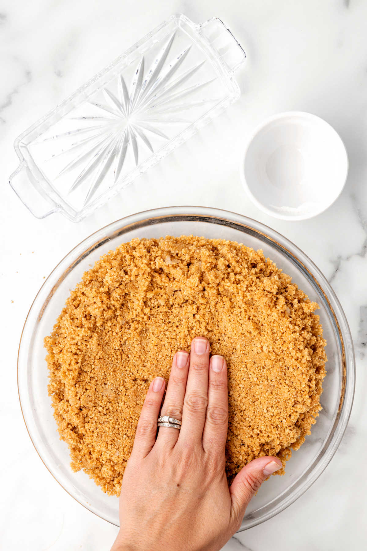 A hand patting graham cracker crumbs into a pie pan.