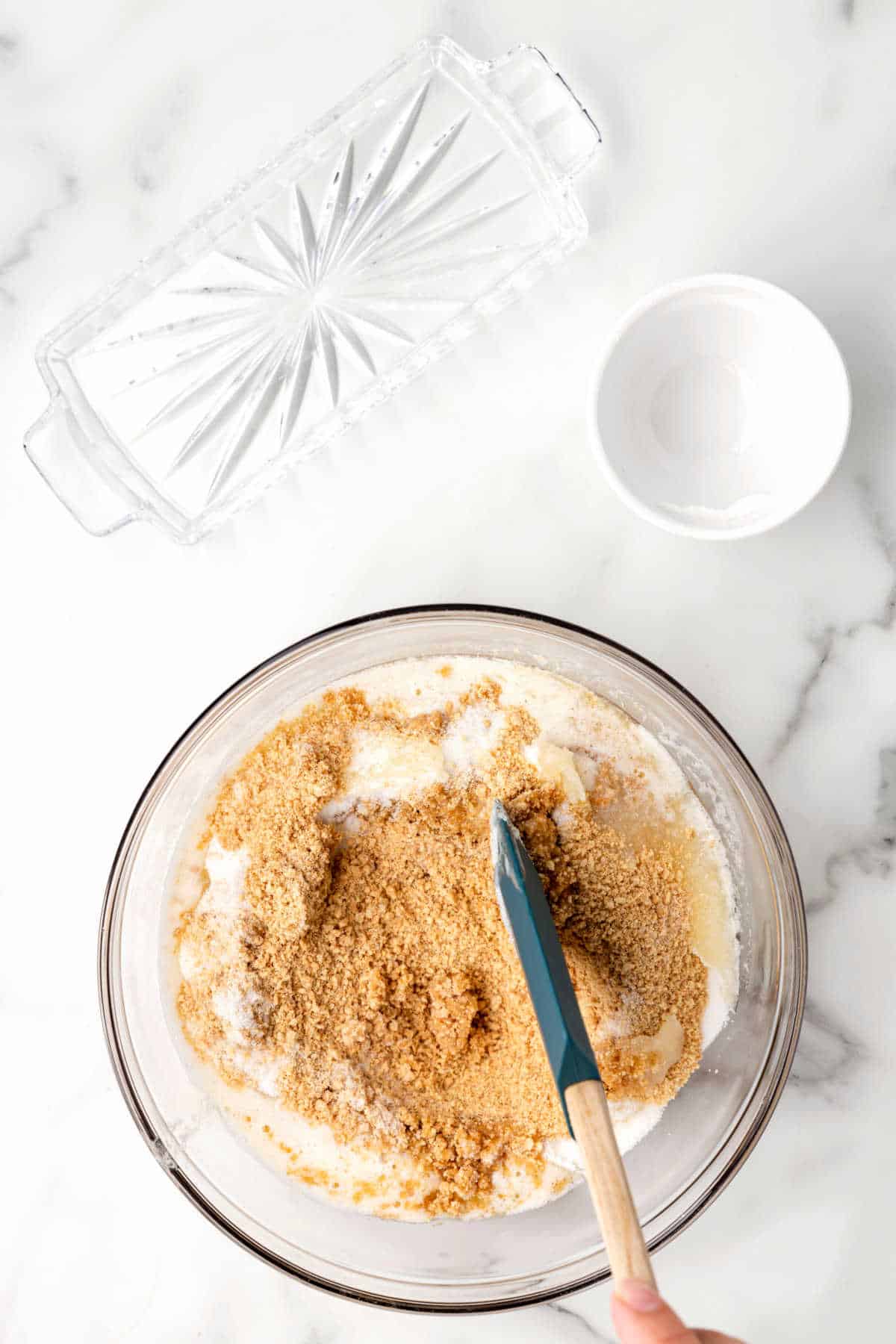 A rubber spatula stirring butter graham cracker crumbs and sugar together.