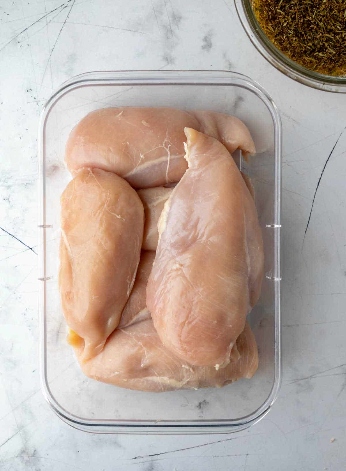 Raw chicken in a container next to a dish of marinade. 