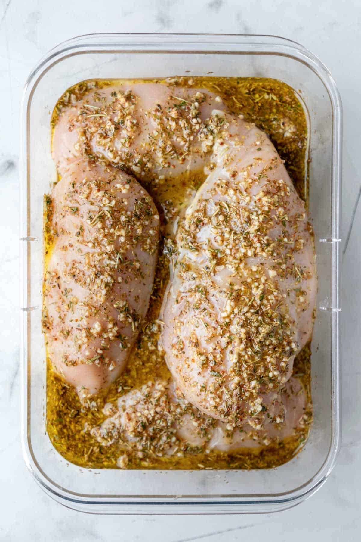 Greek chicken marinade on raw chicken in a container.