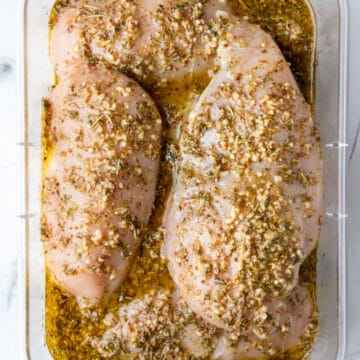 Raw chicken breast in Greek marinade in a container.