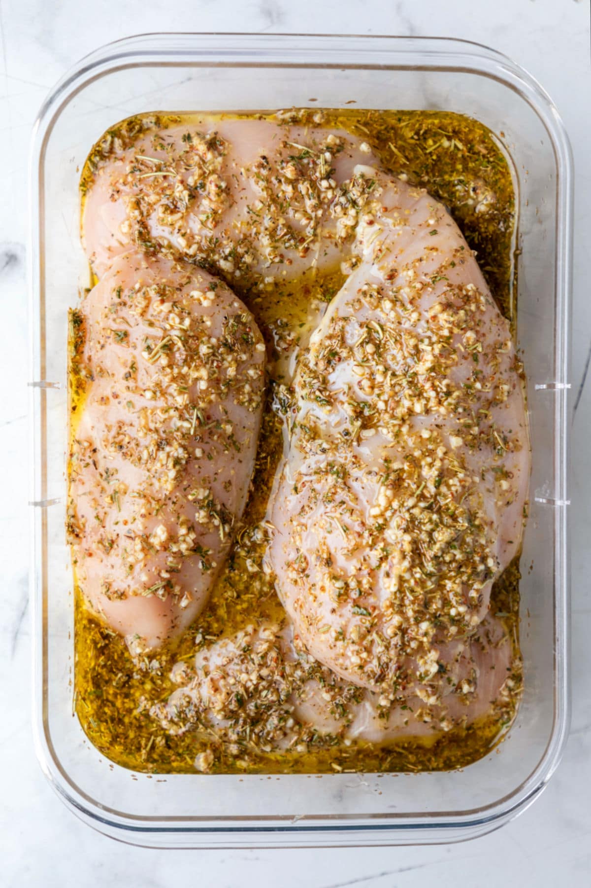 Raw chicken breast in Greek marinade in a container. 