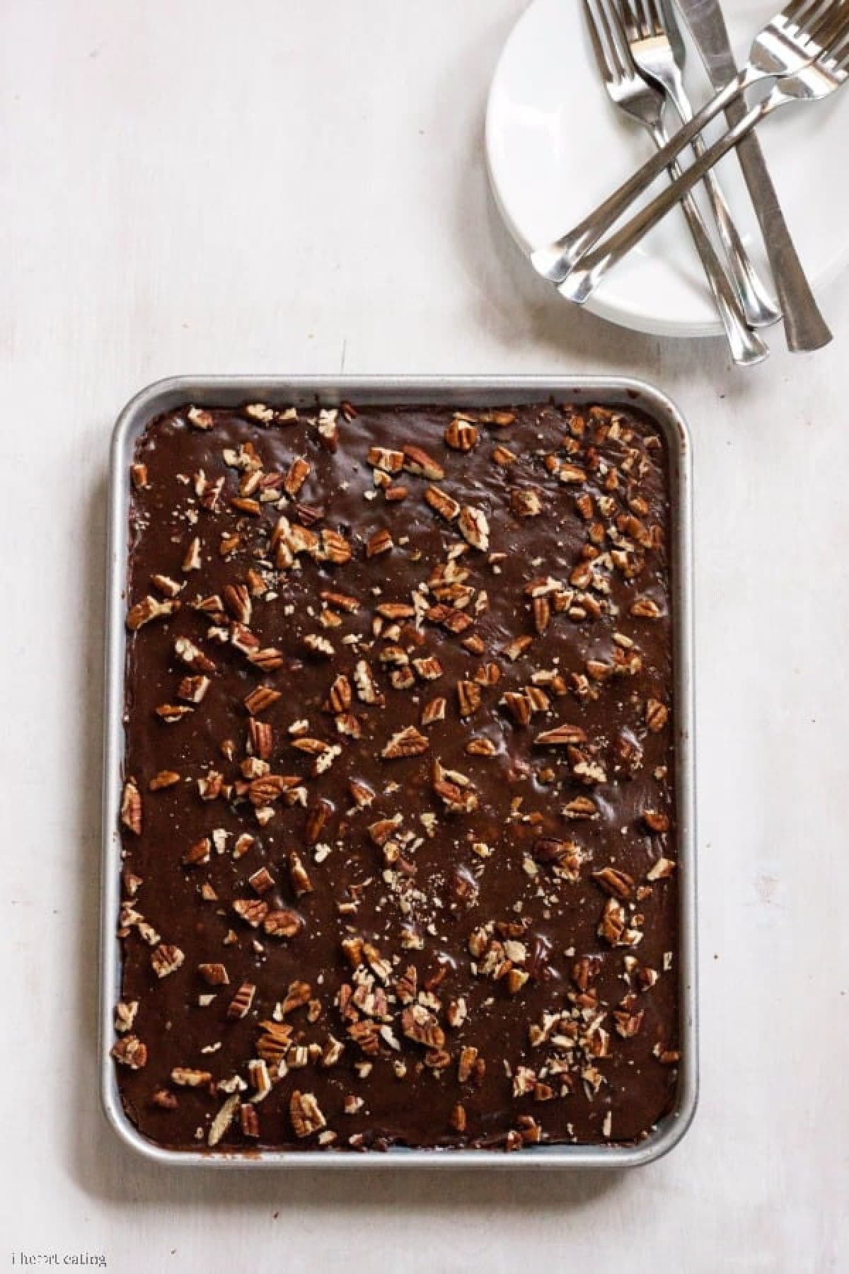 Chocolate Sheet Cake in a pan next to a plate with silverware.