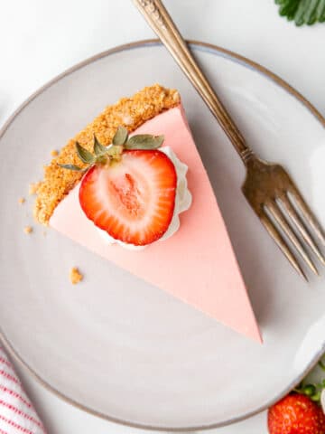 A slice of strawberry jello pie topped with whipped cream and a sliced strawberry.