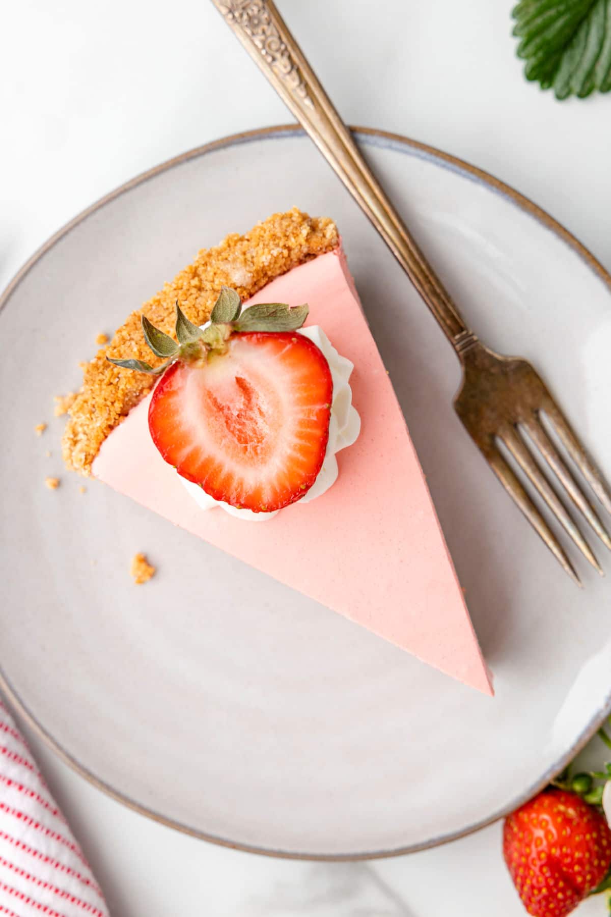 A slice of strawberry jello pie topped with whipped cream and a sliced strawberry.