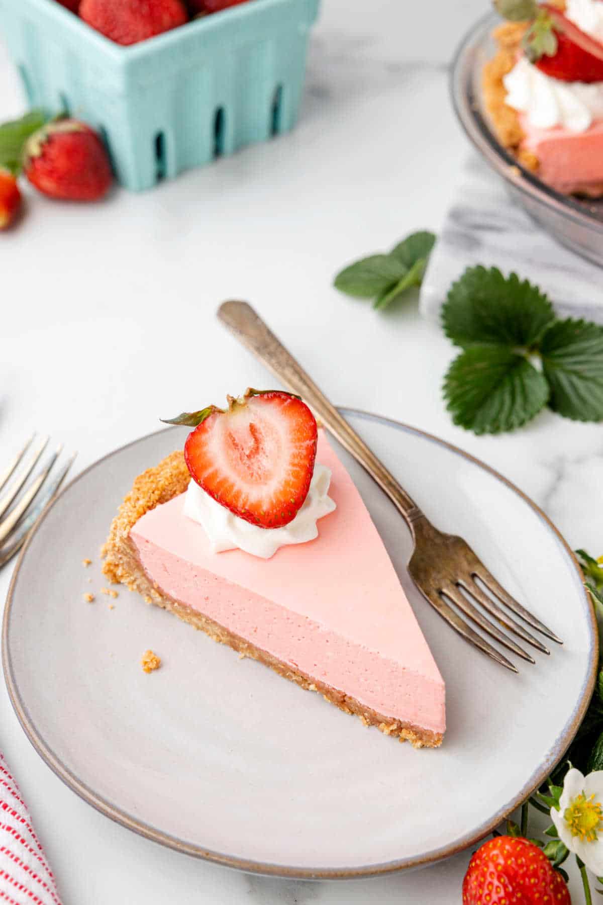 A slice of strawberry jello pie next to a container of strawberries. 