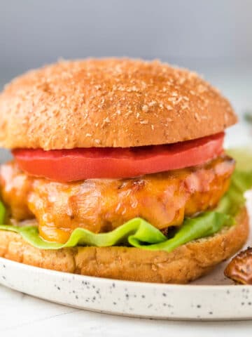 Square photo of a turkey burger on a whole wheat bun with lettuce and tomato.