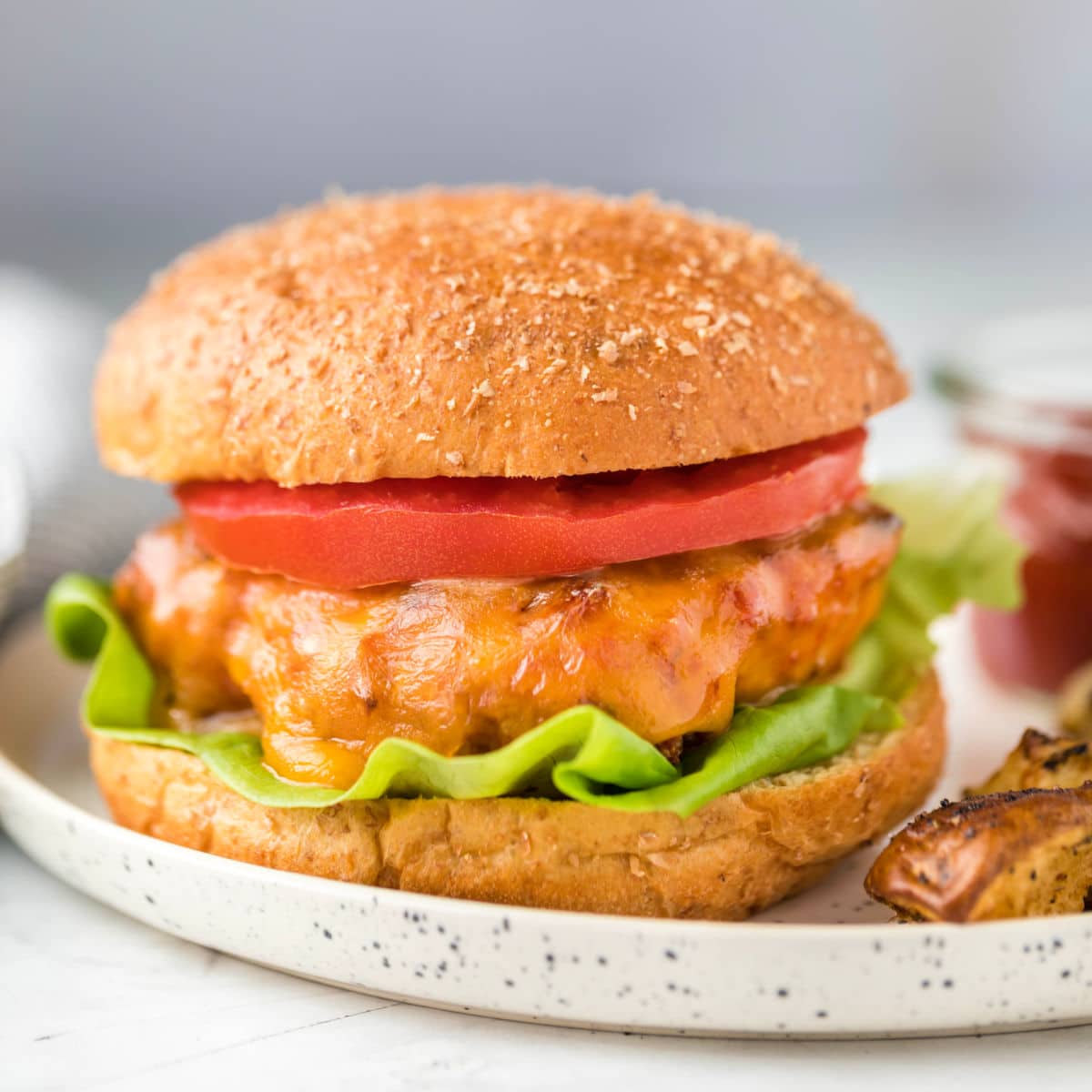 Square photo of a turkey burger on a whole wheat bun with lettuce and tomato.