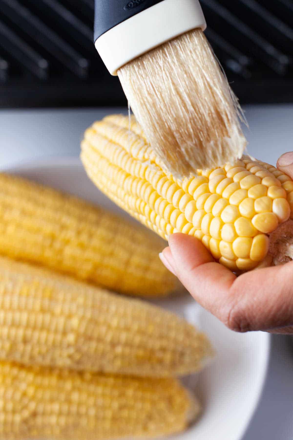 A basting brush brushing butter onto corn. 