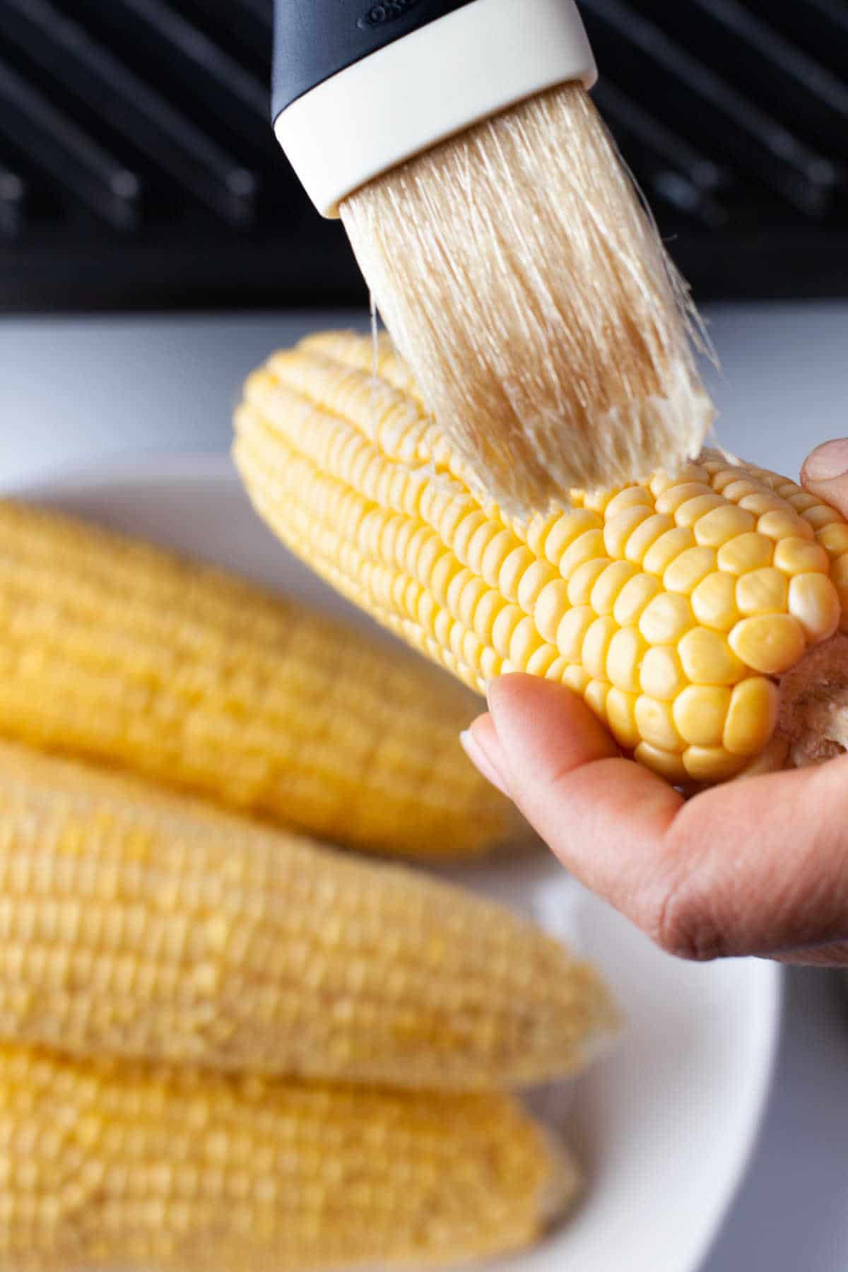 A basting brush brushing butter onto corn.