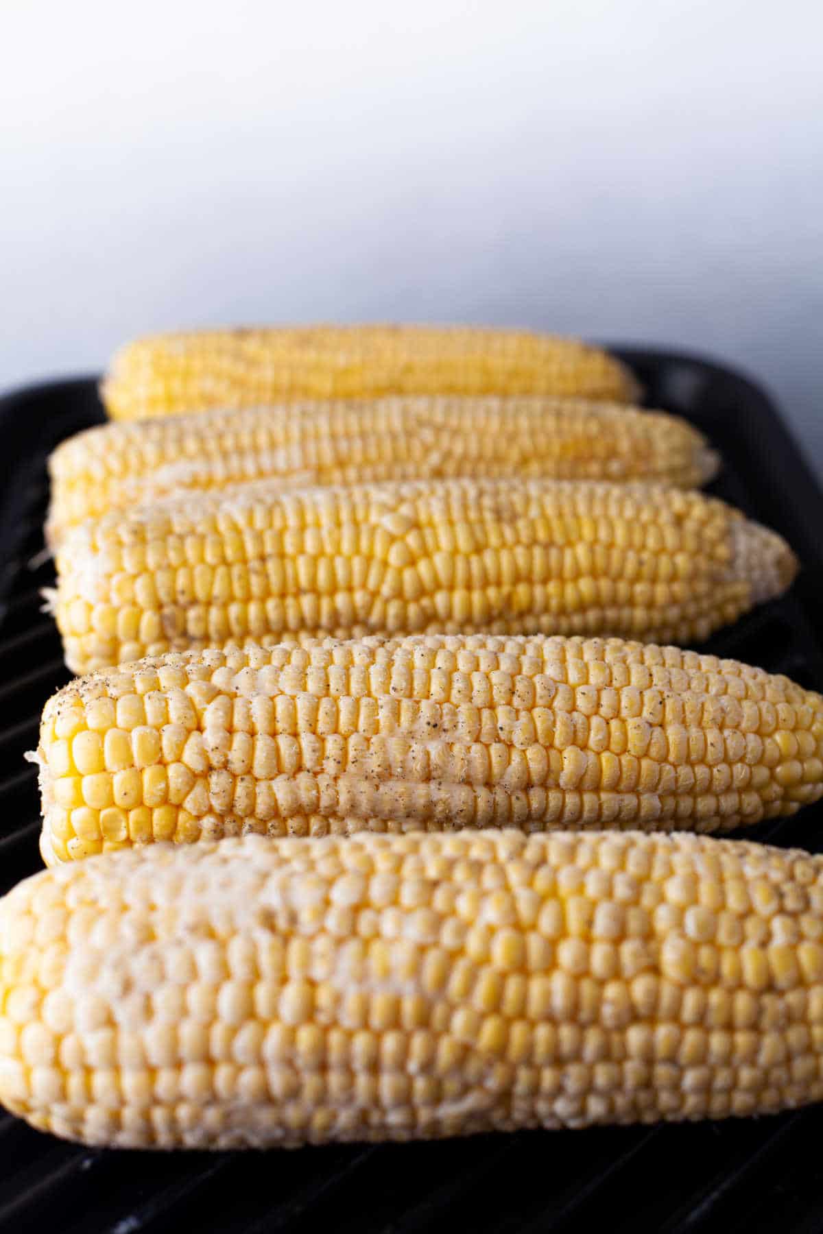 Ears of corn grilling on a grill pan.