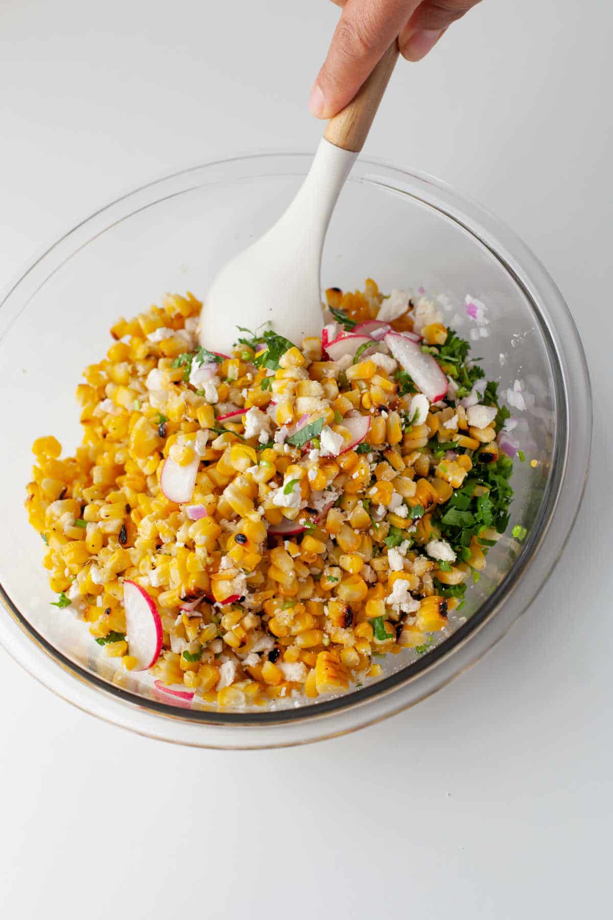 A white spoon mixing up Mexican street corn salad.