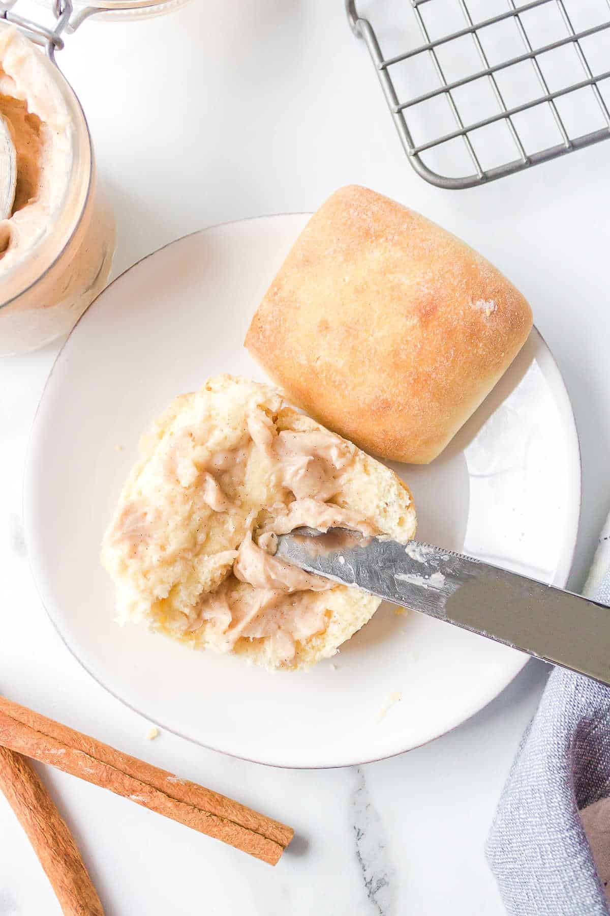 A knife spreading cinnamon honey butter on a roll. 