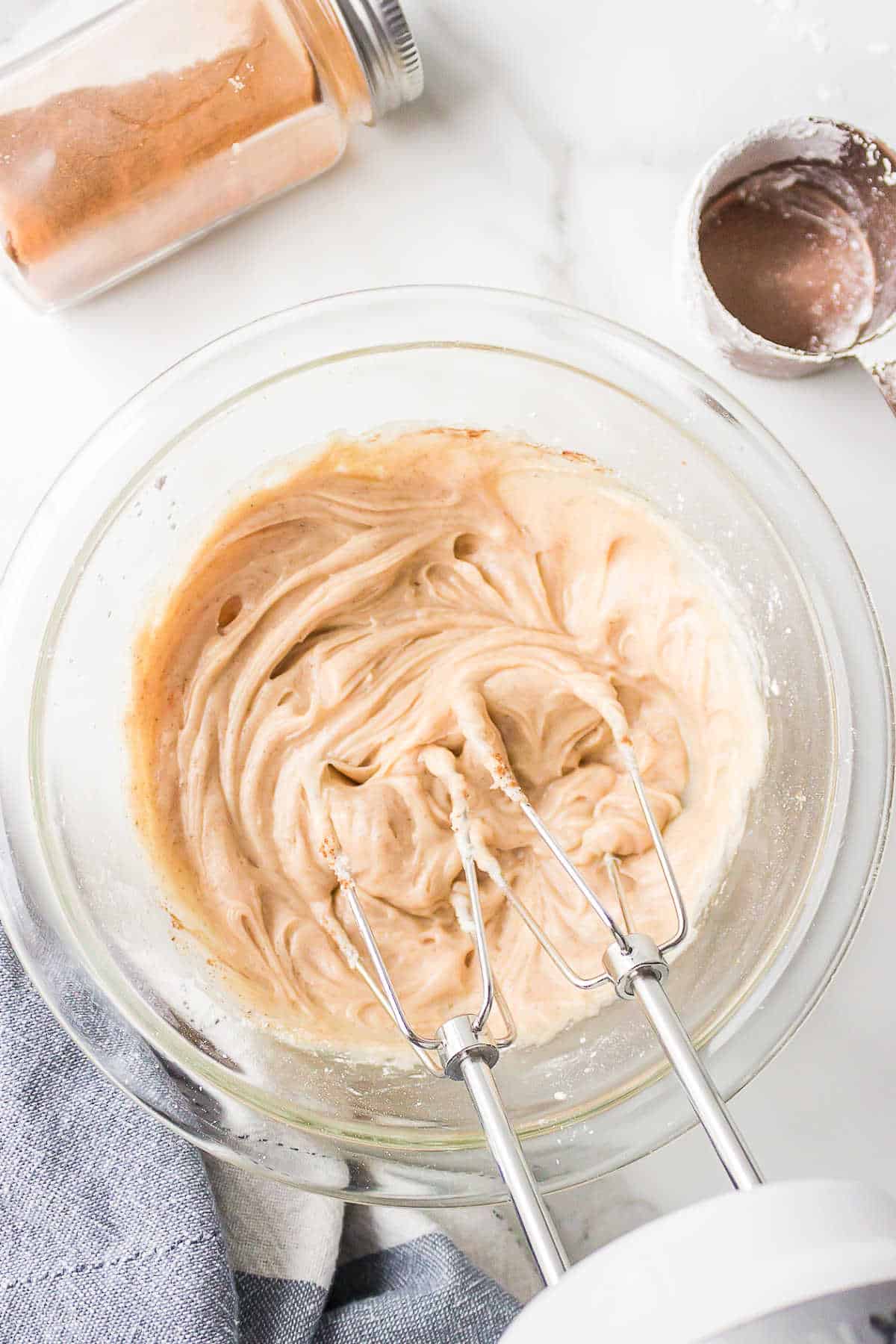 An electric hand mixer beating cinnamon butter in a mixing bowl.
