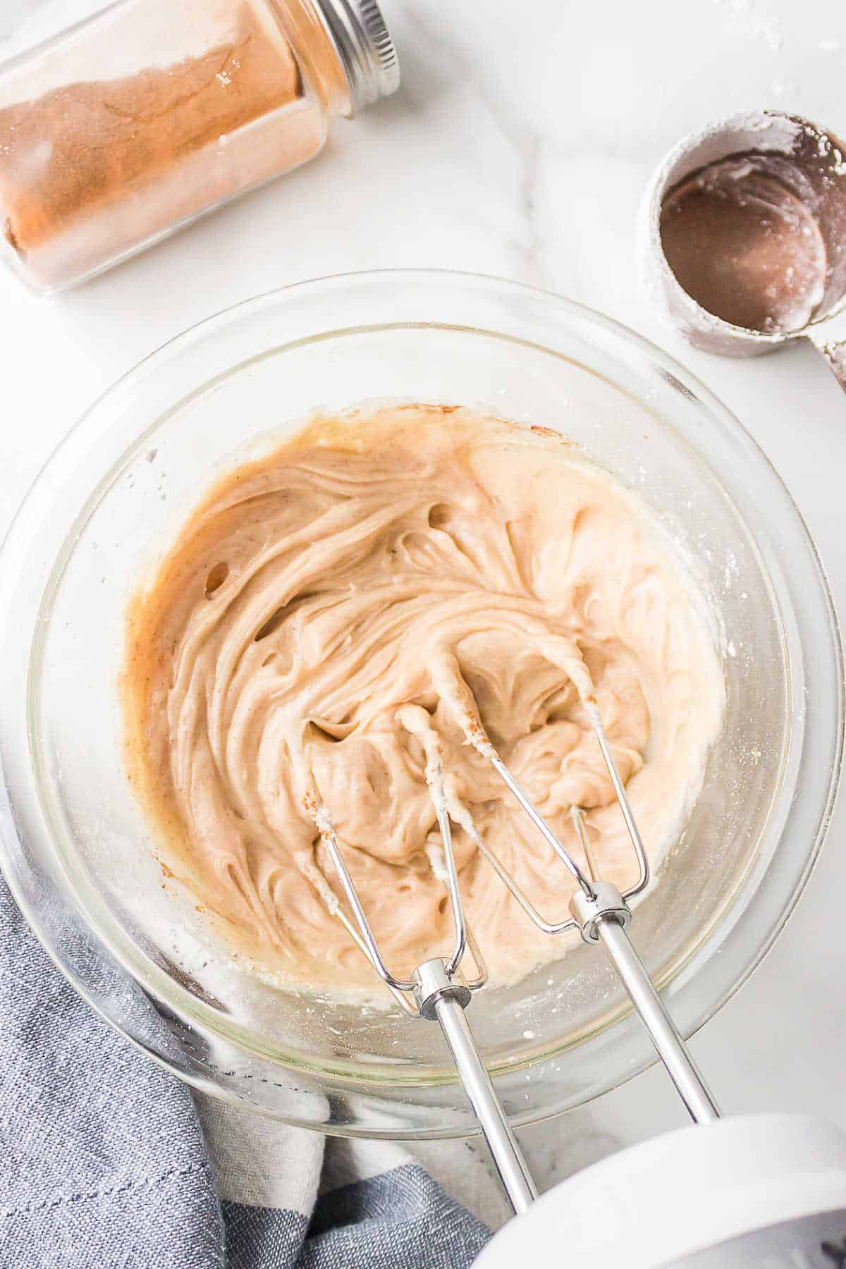 An electric hand mixer beating cinnamon butter in a mixing bowl. 