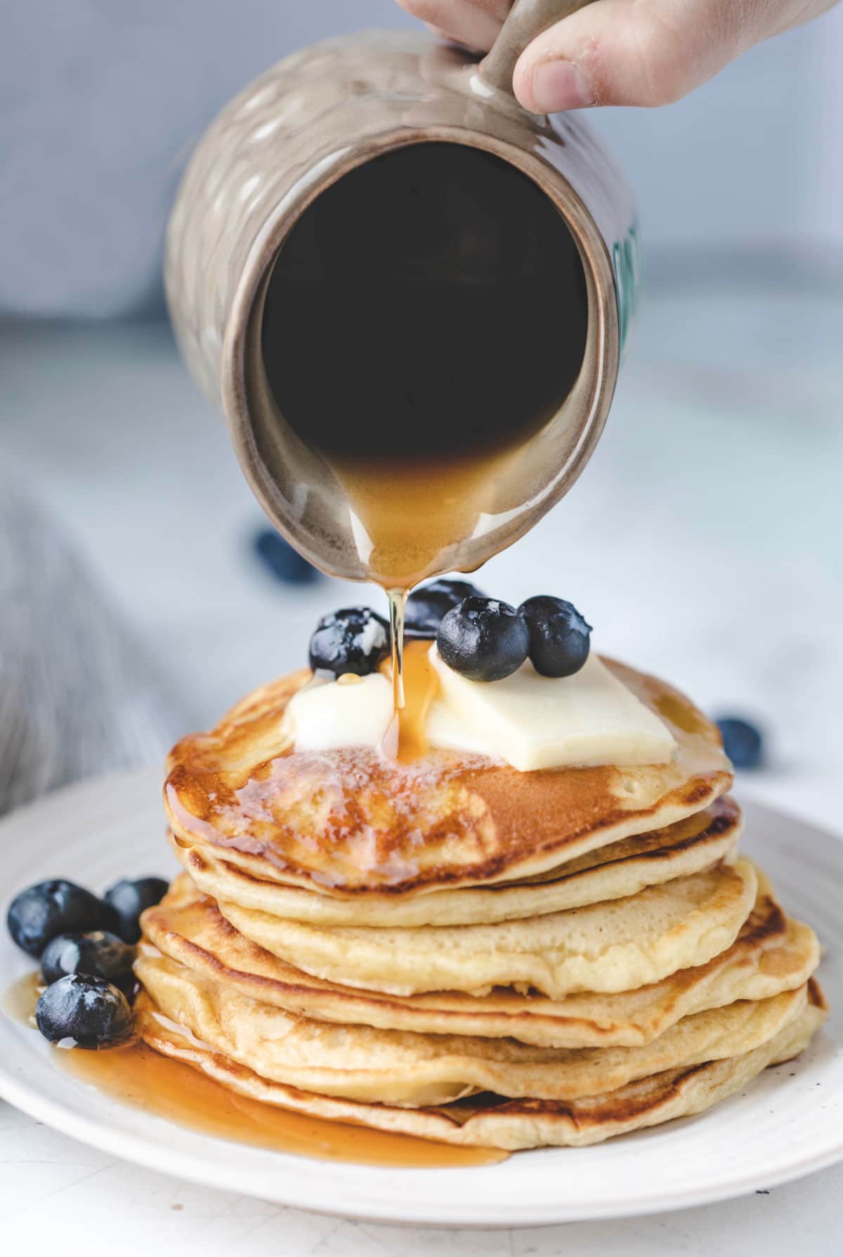 Maple syrup pouring onto a stack of blueberry pancakes. 