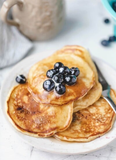 Plate of blueberry pancakes topped with butter and fresh blueberries.